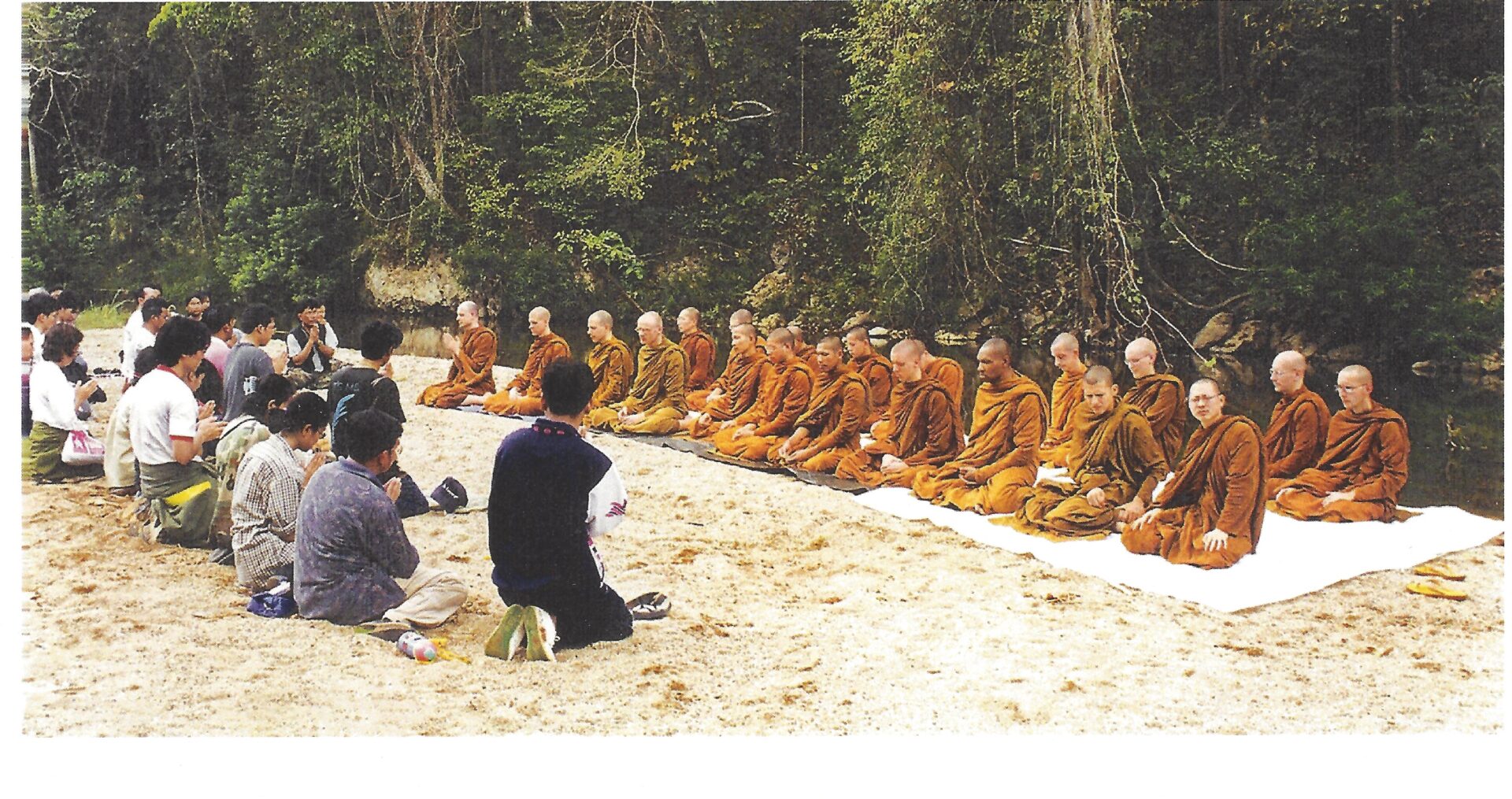 A group of people sitting on the ground with monks.