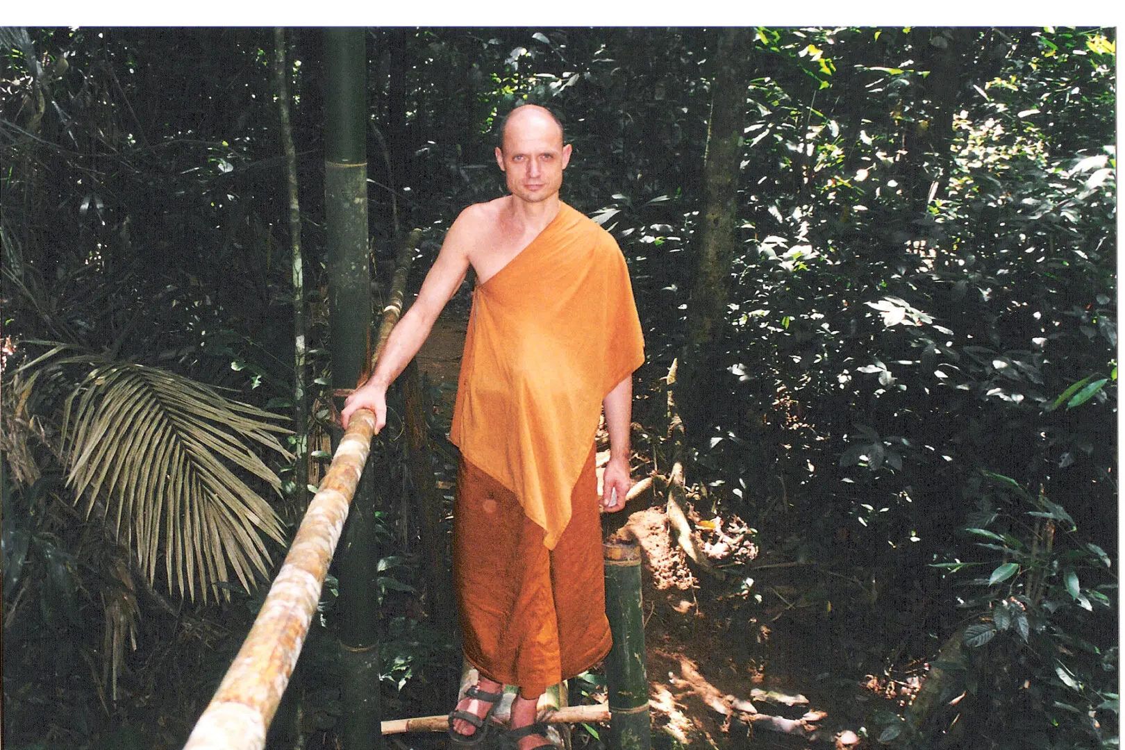 A man in an orange robe standing on a wooden stick.