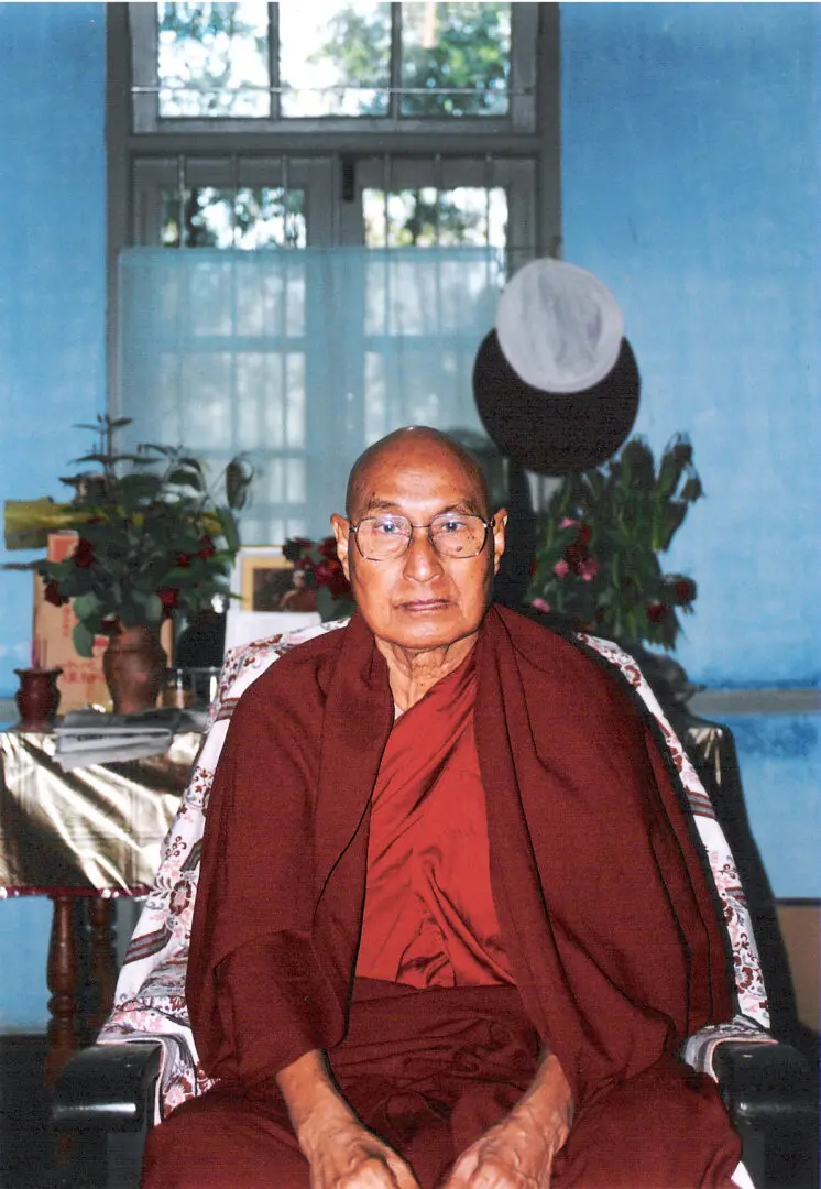 A man in red robe sitting on chair with blue walls.