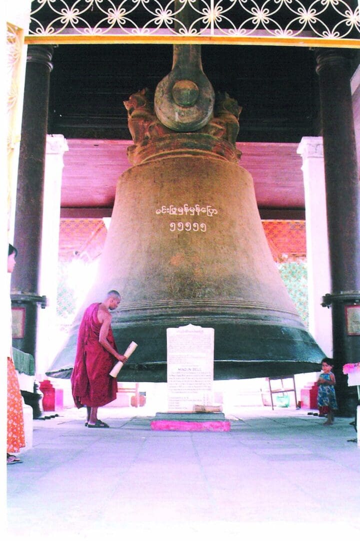 Monk standing by a giant ancient bell.